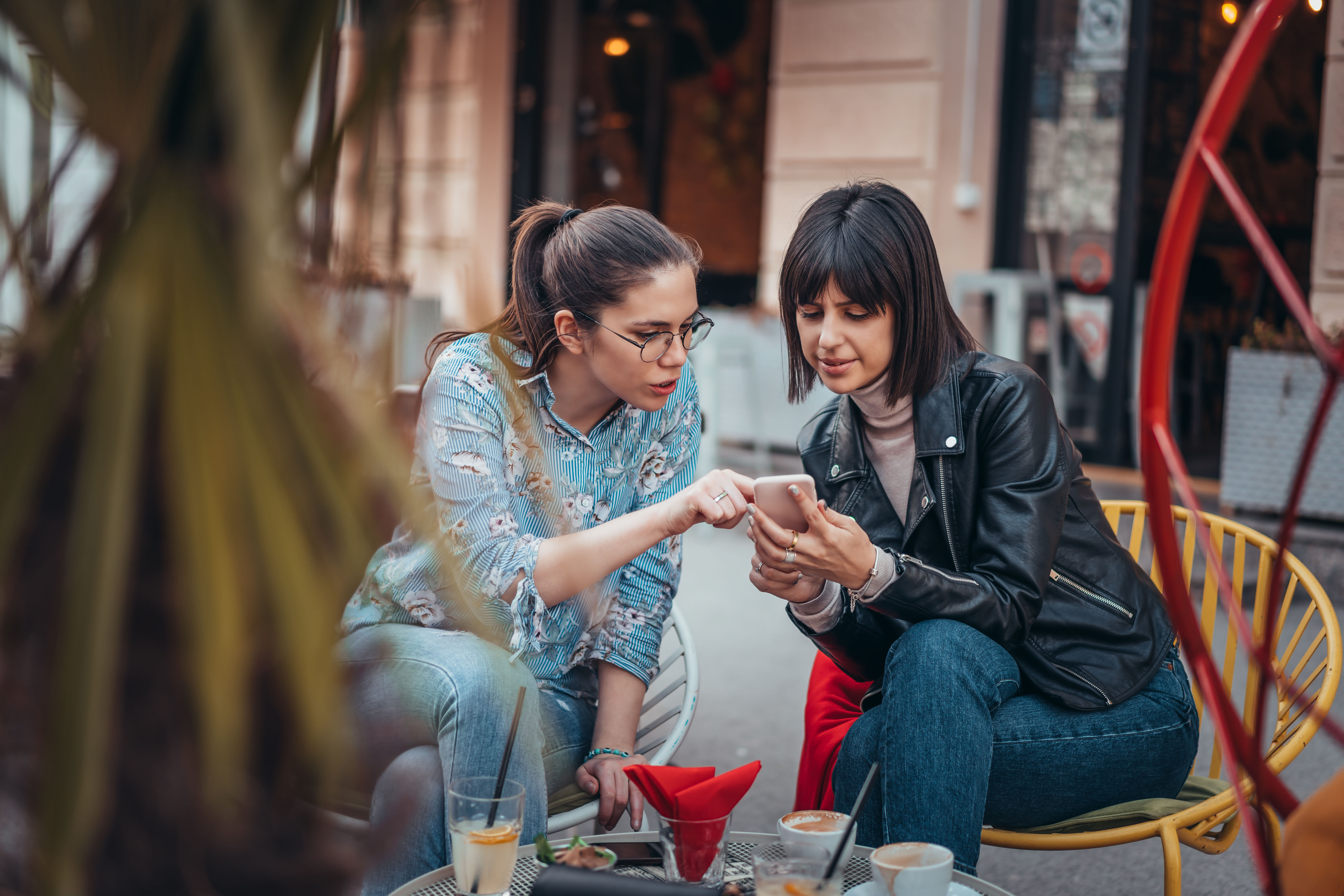 Two women with rings discuss something on a phone while eating at an outdoor table